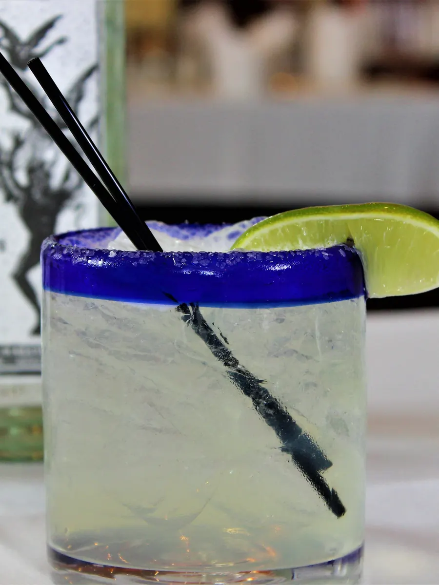 A margarita on the rocks in a blue-rimmed glass with lime